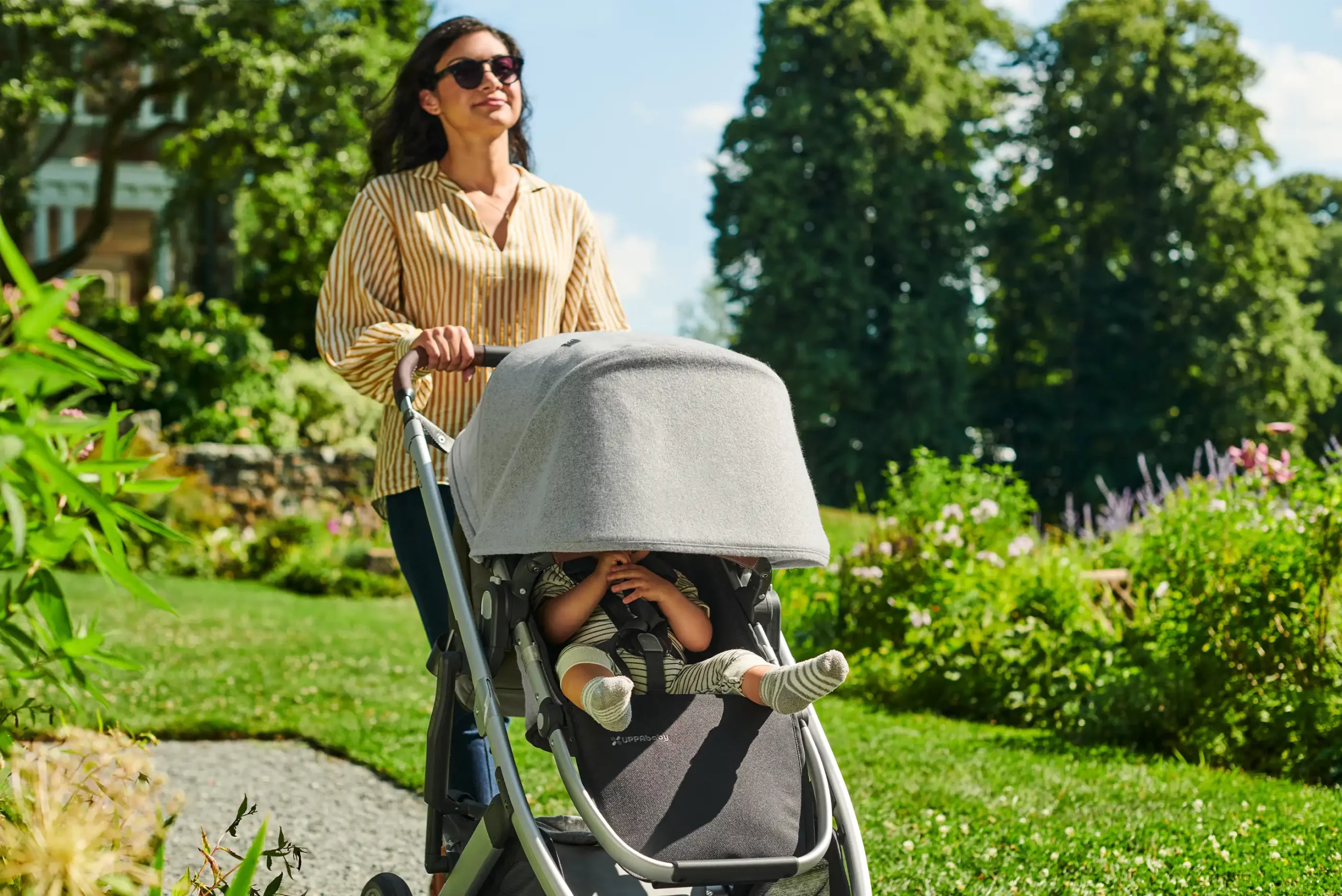 A child is pushed by a smiling woman on a sunny day in the included Toddler Seat with the help of an extended Cruz canopy that shields the child from harmful UV rays