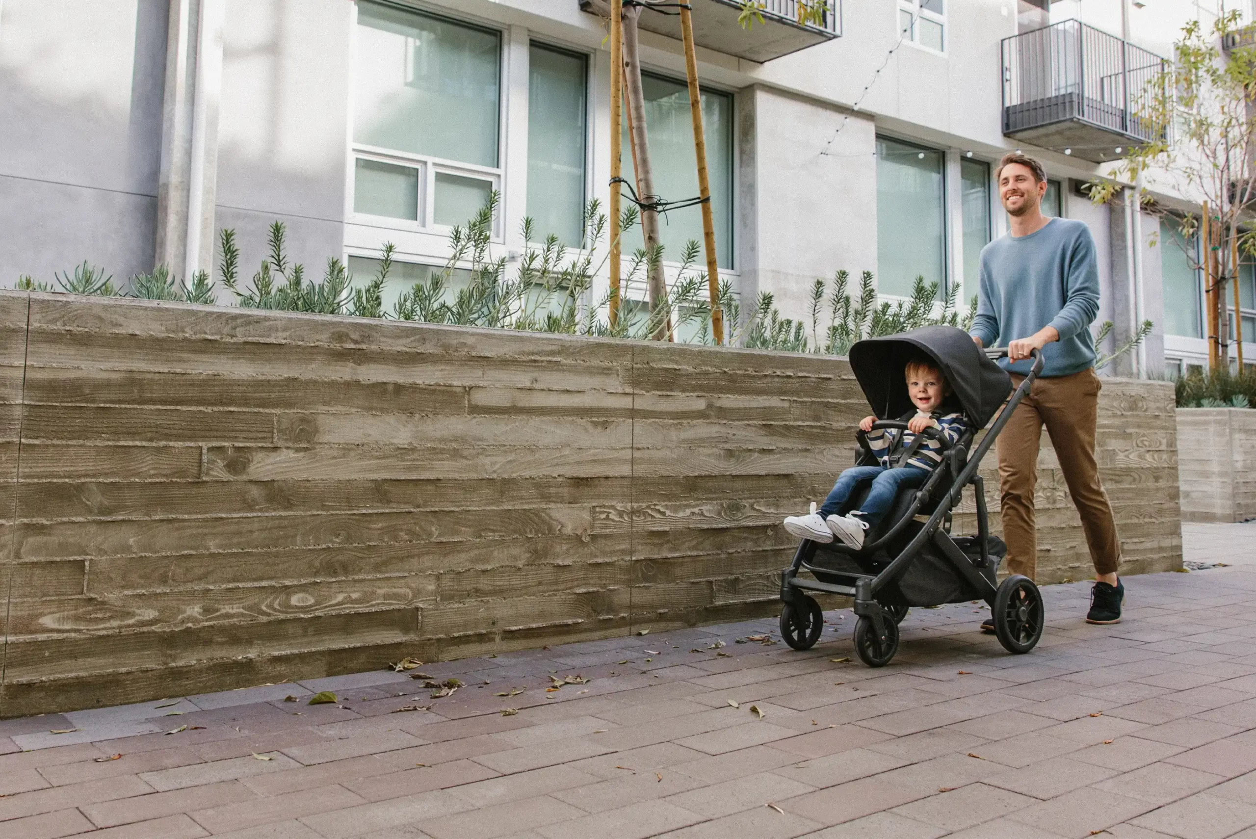 A child is pushed by a smiling woman along a brick path while staying comfortably secure due to the Cruz V2's all-wheel suspension + independent shocks