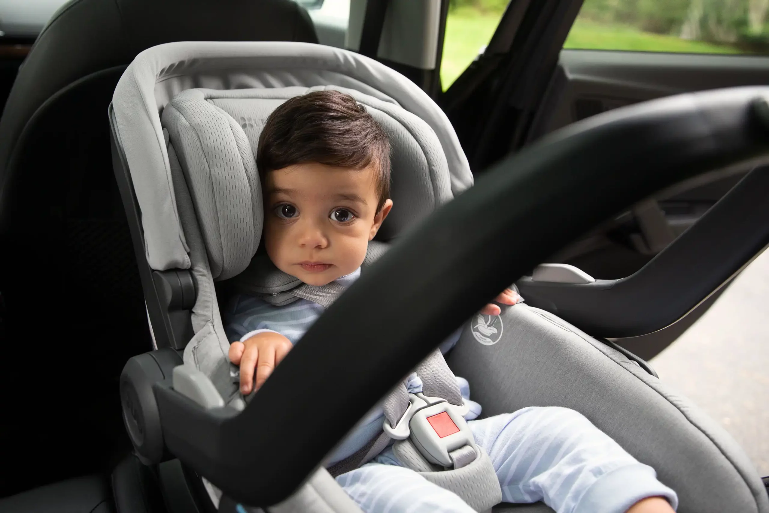 An adorable child looks at the camera, safely secured in the Mesa V2 infant car seat, with the carriers carry handle deployed in its 4th anti-rebound handle position for increased safety in rebound & rear-impact collisions