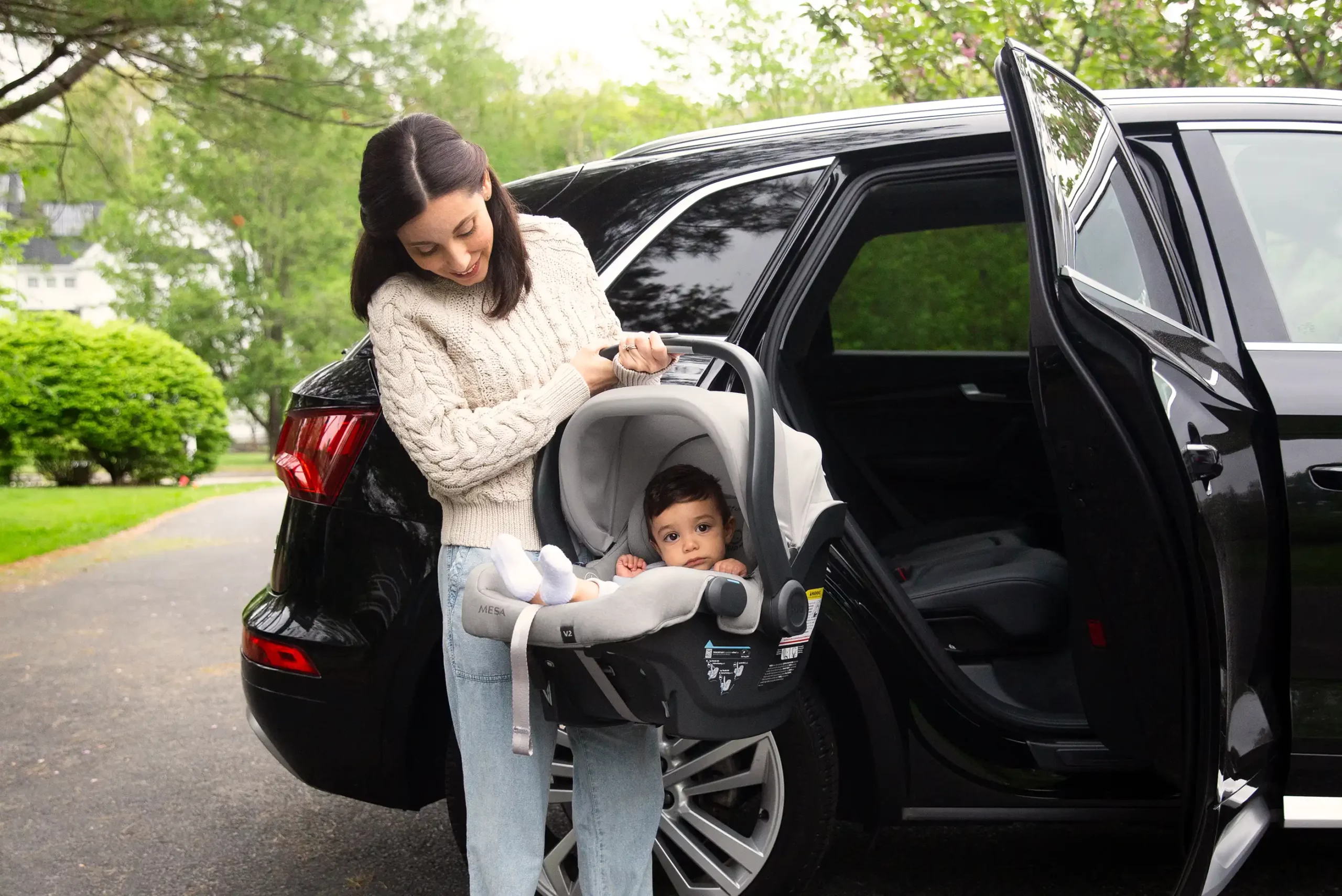 A woman removes her child in the Mesa V2 from her car, deploying the large, UPF 25+ hideaway canopy for use on a sunny day