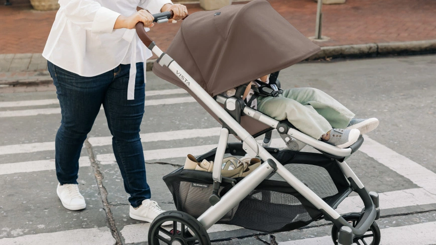 A smiling woman comfortably pushes her child on a brick city sidewalk, using the Vista's all-wheel suspension and shock absorbers