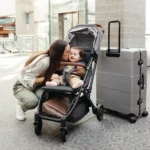A smiling toddler is comfortably secured in the Minu V2's five-point, no rethread harness while on-the-go in an airport