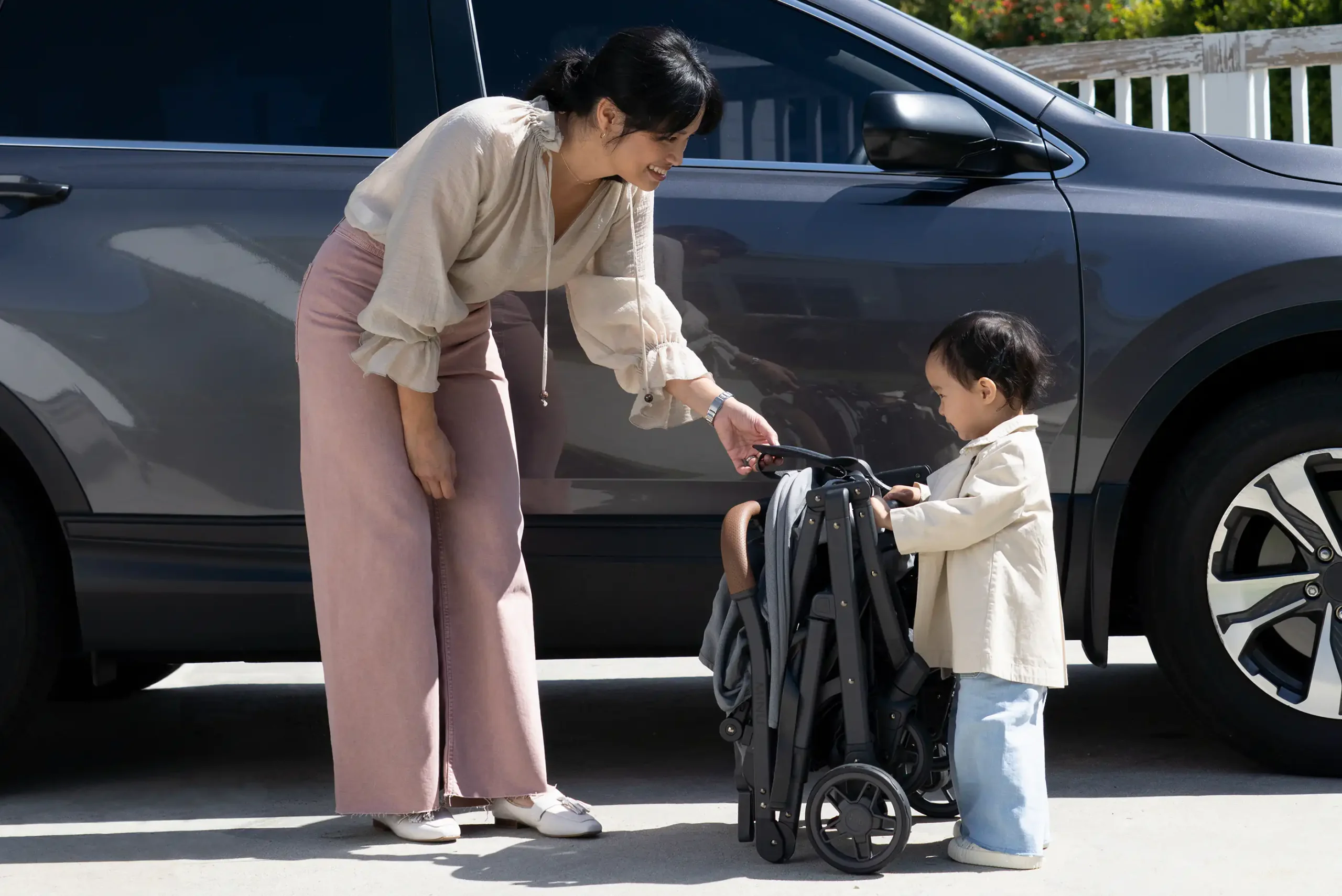A smiling woman and her toddler stand near a compactly folded Minu V2, ready to load it effortlessly into their car for a travel excursion