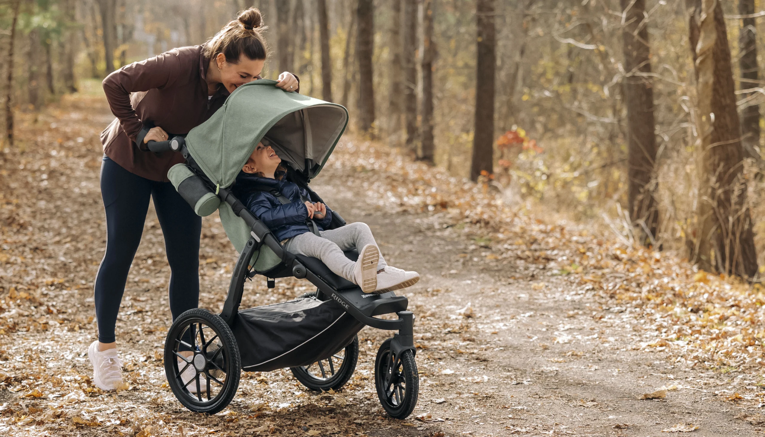 A woman smiles at her child through the Ridge's mesh canopy window while she runs comfortably due to the stroller's advanced suspension two-stage system