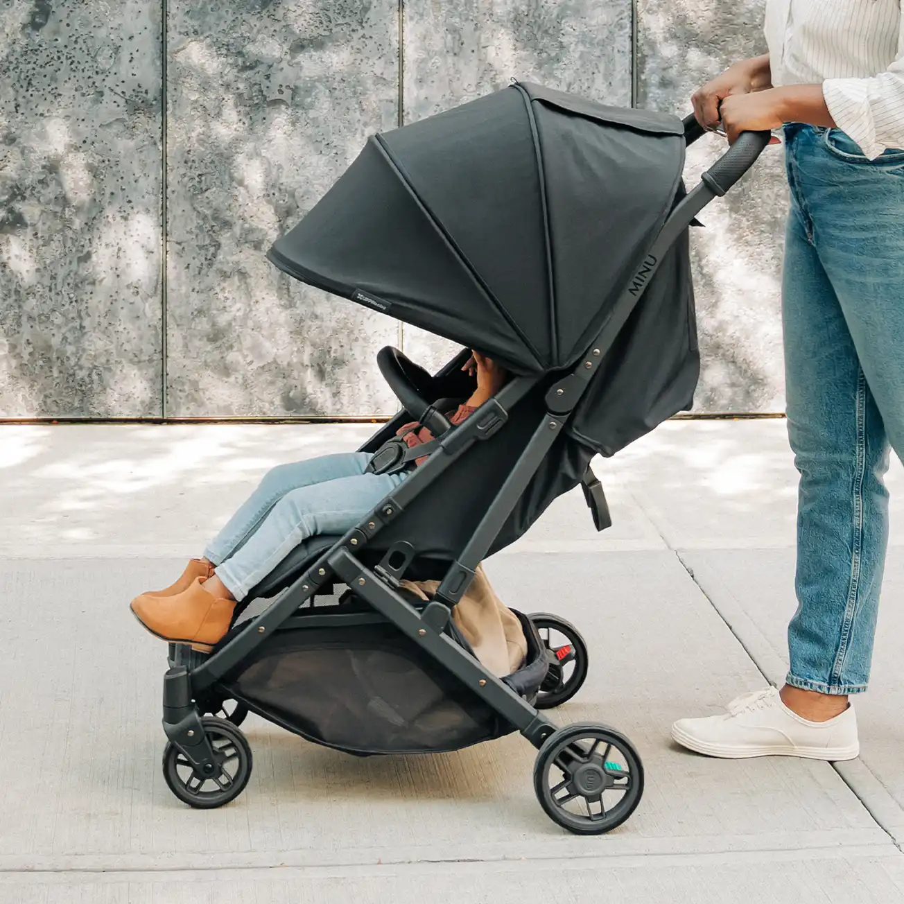 A woman pushes her toddler sitting comfortably in the Minu V2 thanks to its zip-out extendable UPF 50+ canopy