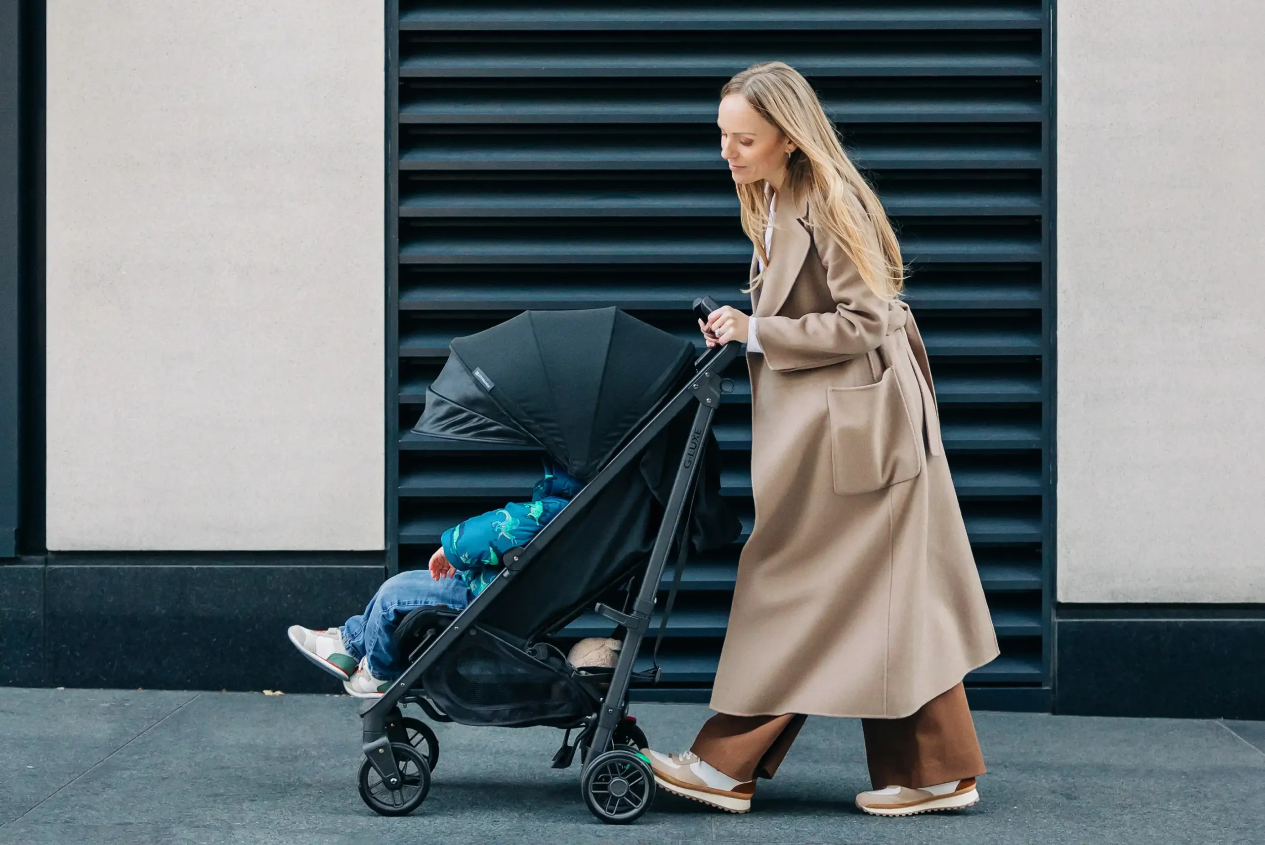 A mom pushes her child comfortably relaxing in the G-Luxe Stroller thanks to its reclining seat and extra large canopy for sunny days
