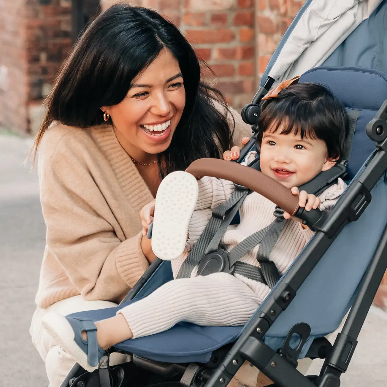 A happy woman looks at her smiling toddler in a Minu V2 stroller who sits comfortably due to its 5-point, no rethread harness, and adjustable leg rest