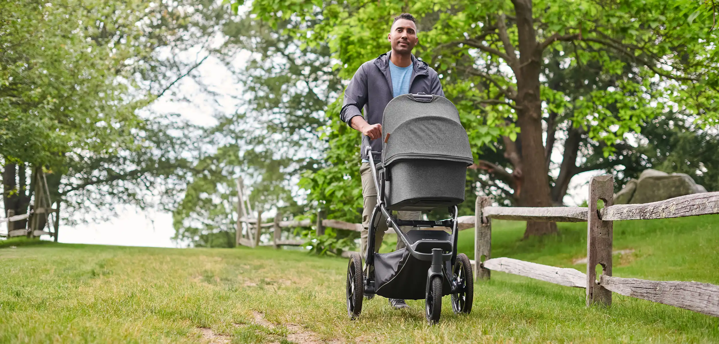A man comfortably pushes the Ridge stroller through a pasture, using adapters and the Bassinet accessory to convert the stroller to a from-birth option
