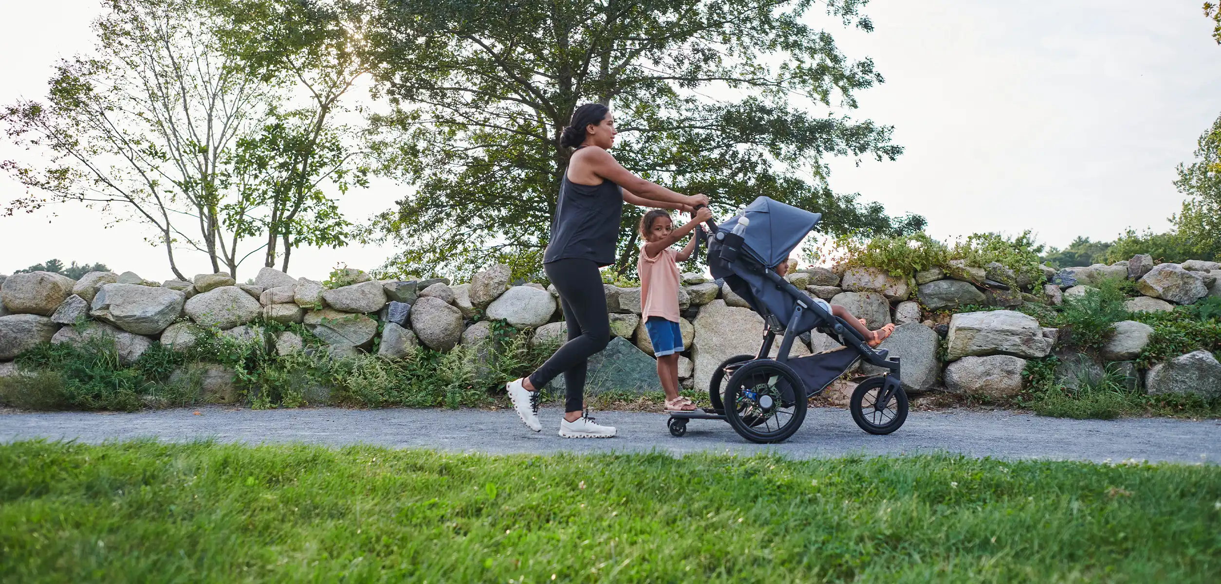 A woman jogs with her two children, one relaxing comfortably in the Ridge, while the other glides along with the help of the Piggyback Accessory that attaches directly to the stroller