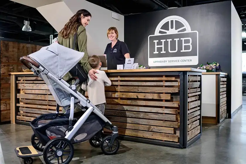 A parent and their child visiting a Hub Service Center in an UPPAbaby Vista V2 stroller - Anthony | white and grey chenille | carbon frame | chestnut leather.