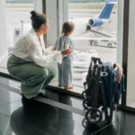 A child watches the airplanes on the runway of the airport, and while the stroller is not in use, it stands on its own to the side after a one-handed fold