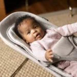 A smiling baby comfortably bounces in the Mira 2-in-1 bouncer, secured by the adjustable padded harness while staying cozy with the included seat liner