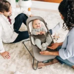 A smiling baby comfortably bounces in the Mira 2-in-1 bouncer, secured by the adjustable padded harness while staying cozy with the included seat liner