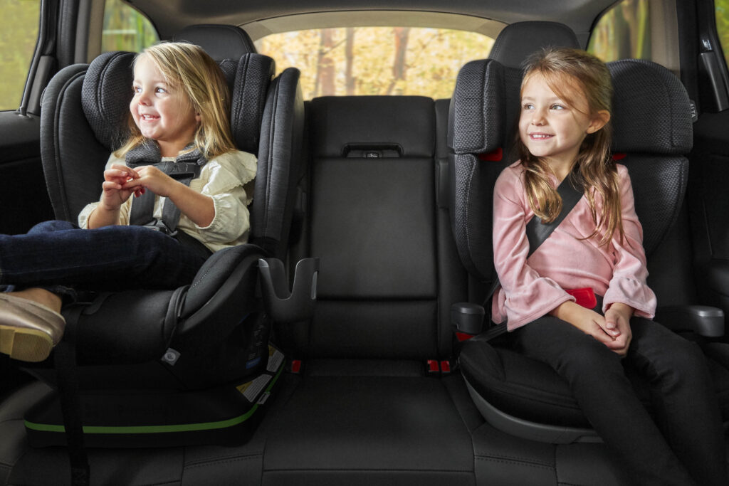 Two children smiling and secured in an UPPAbaby Knox Car Seat and an Alta Booster Seat, showcasing the advanced safety features and comfortable design.