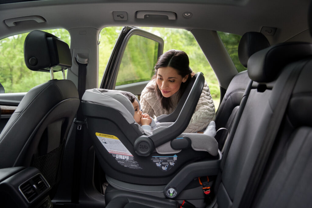 A caring mother attentively buckles her child into the UPPAbaby Mesa car seat, highlighting the seat's secure and nurturing design.