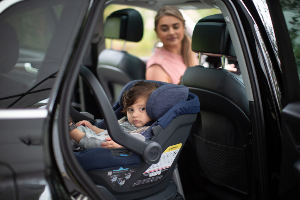 A little one safely secured in his UPPAbaby Mesa Max Infant Car Seat, with mom carefully looking on.