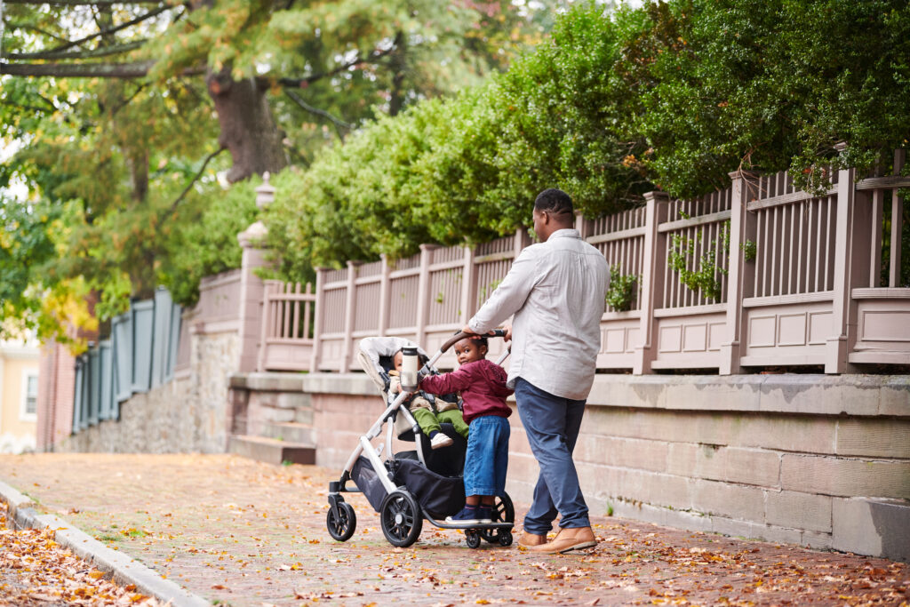Father and child enjoying an autumn day with an UPPAbaby Vista V2 stroller and PiggyBack board, emphasizing ease of use and family-friendly design in an urban setting