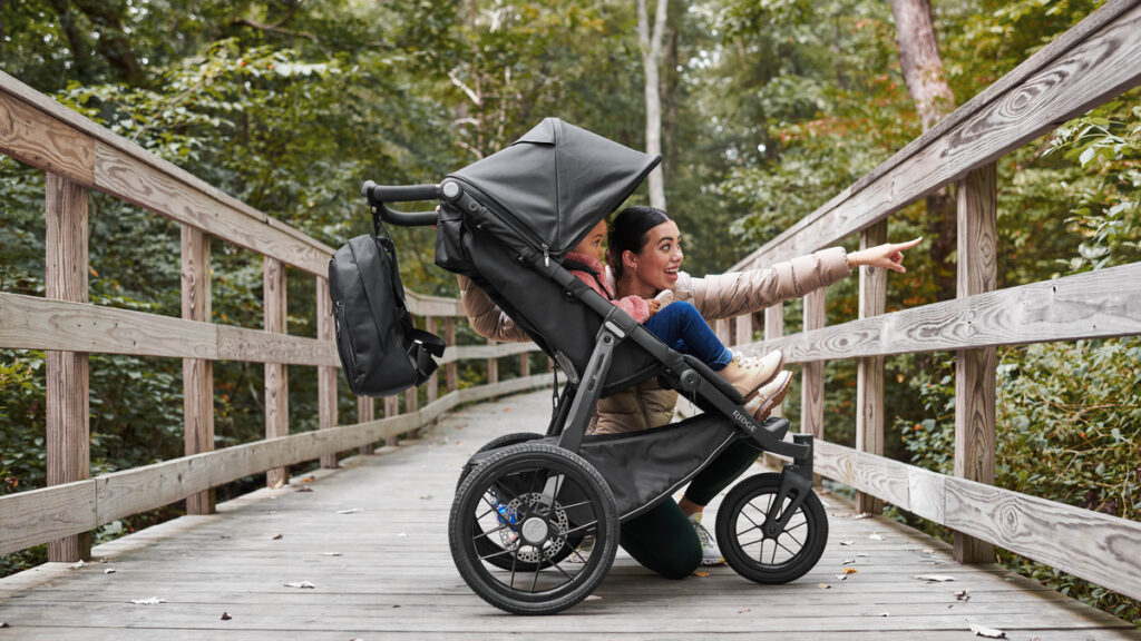 RIDGE jogging stroller in Jake Black with an attached changing backpack, displayed on a wooden bridge, emphasizing the stroller's outdoor readiness and storage solutions.