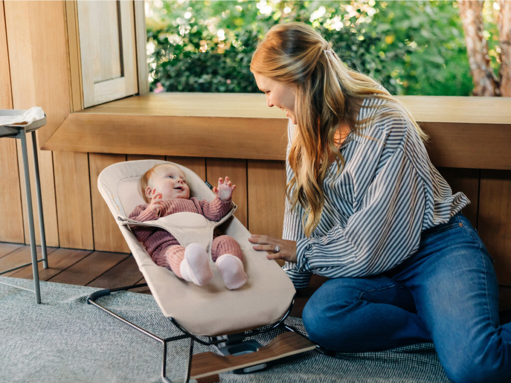 A infant bounces in the Mira bouncer secured with the adjustable harness as their mom smiles