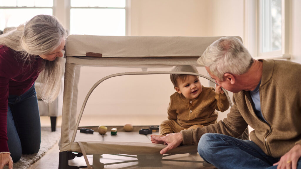 A baby plays with their grandparents in the Remi playard with easy access provided by Remi's zip open soothing panel