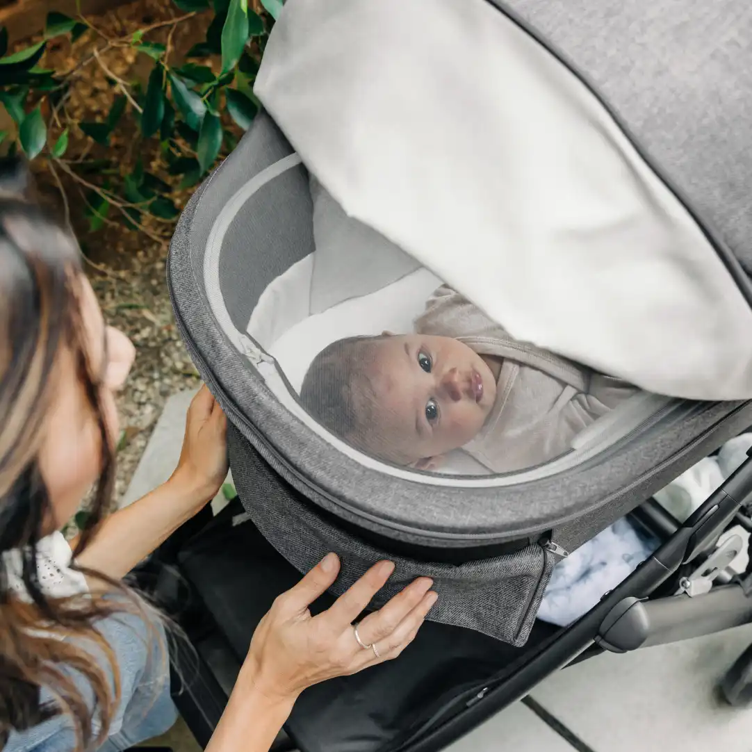 Mom strolling with Vista V3 kneeling down to view infant laying in Bassinet through cross ventilation panels