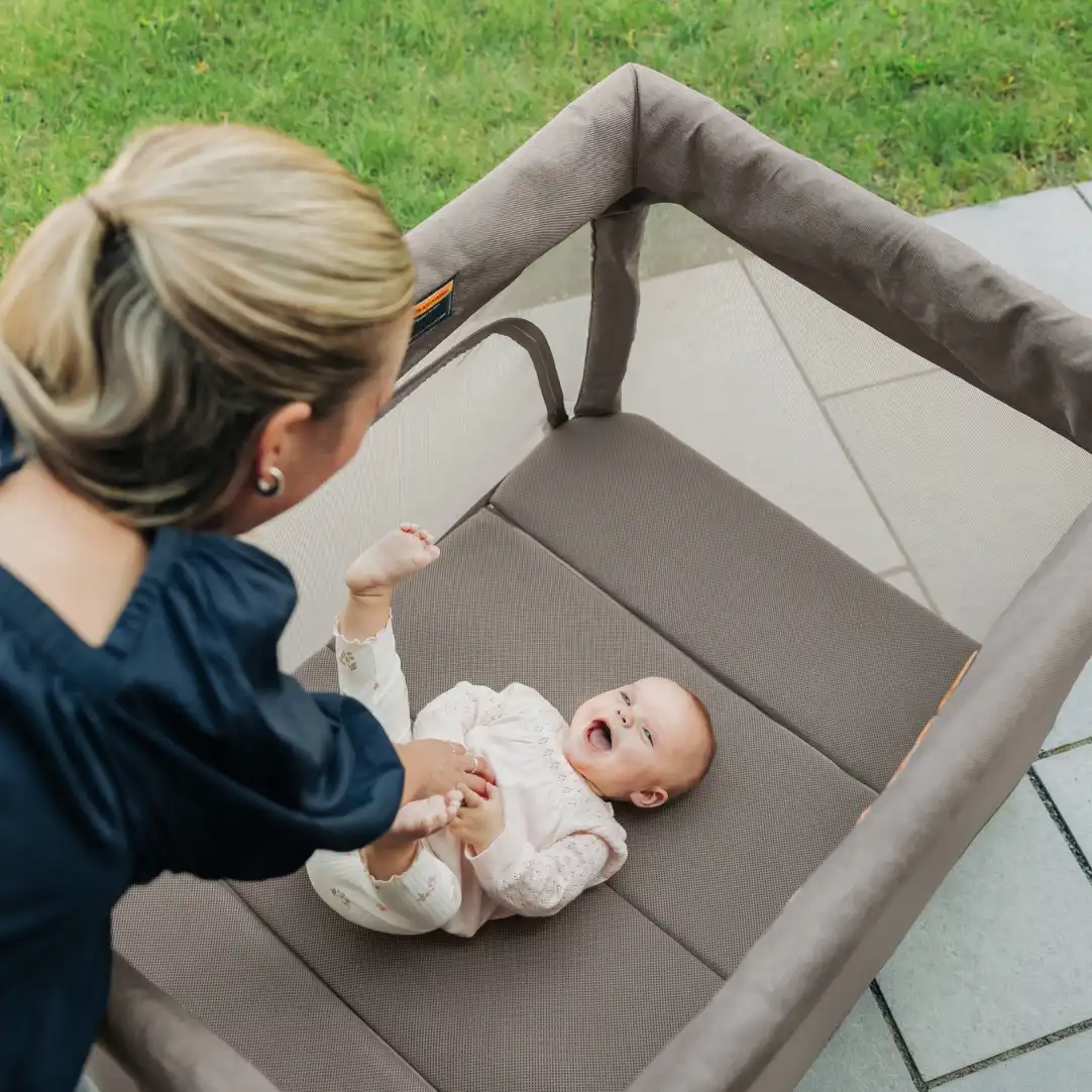 A parent plays with their child who is smiling while laying in the playard